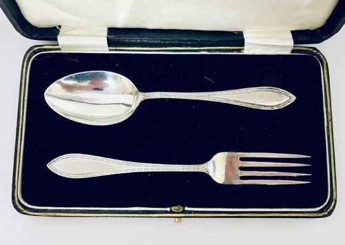 fig 2. An antique silver christening spoon and fork set presented inside an open black fitted case lined with cream silk and dark velvet.
