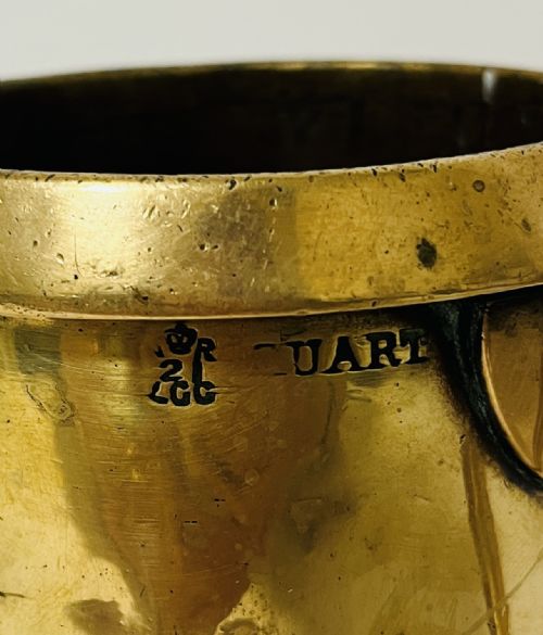 fig 1. A Victorian brass quart tankard with a curved side handle, stamped verification marks near the rim, and a flared base.