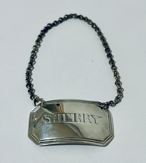 fig 1. A rectangular silver decanter label with chamfered corners, engraved with the word SHERRY and suspended from a fine silver chain.