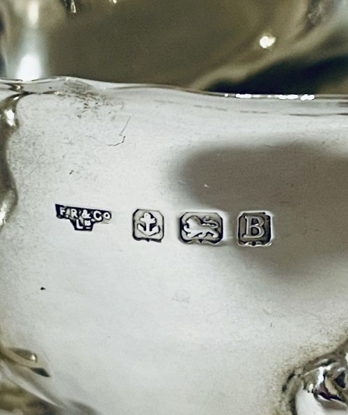 fig 1. A polished sterling silver sauce boat featuring a cut rim, flying scroll handle, shell-capped tripod feet, and visible side hallmarks.