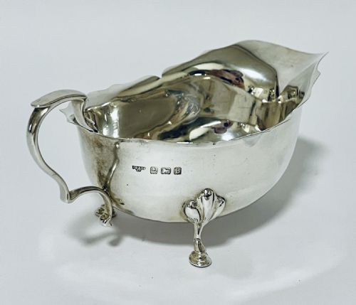 fig 2. A polished sterling silver sauce boat featuring a cut rim, flying scroll handle, shell-capped tripod feet, and visible side hallmarks.