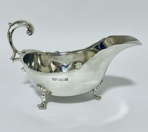 fig 1. A polished antique silver sauce boat featuring a wavy scalloped rim, a double scroll handle, and three shell-capped cabriole feet.