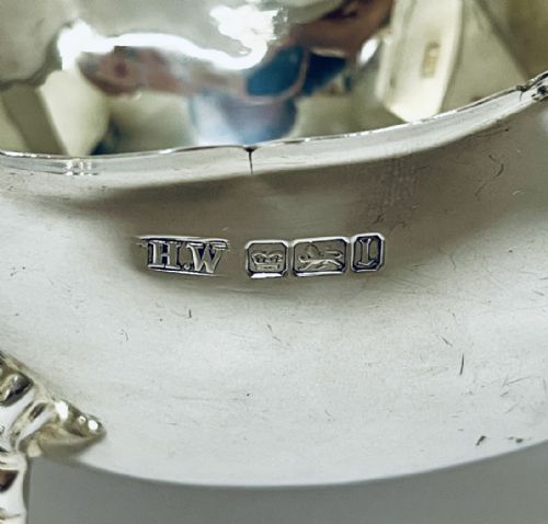 fig 2. A polished antique silver sauce boat featuring a wavy scalloped rim, a double scroll handle, and three shell-capped cabriole feet.