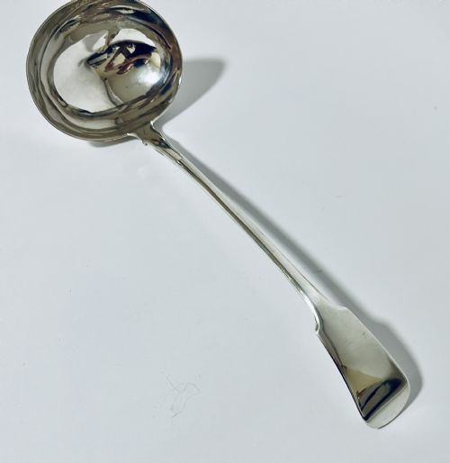 fig 2. A polished Georgian silver serving ladle featuring a deep circular bowl and a long curved handle resting on a plain light surface.