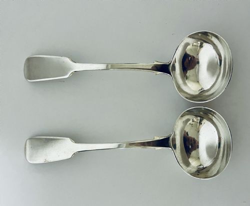 fig 1. A pair of Georgian sterling silver sauce ladles with fiddle pattern handles and deep circular bowls arranged on a plain surface.