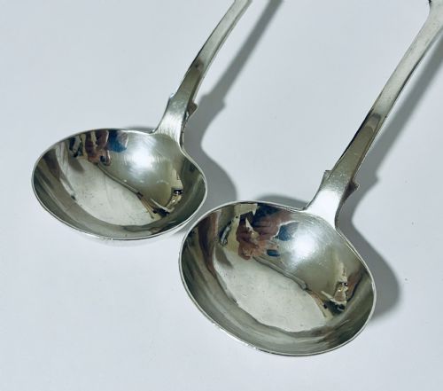 fig 2. A pair of Georgian sterling silver sauce ladles with fiddle pattern handles and deep circular bowls arranged on a plain surface.