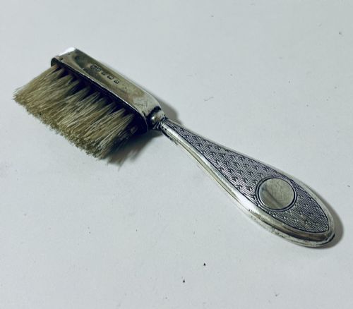 fig 1. An antique silver moustache brush featuring a textured handle with a central circular cartouche and visible silver hallmarks stamped on the brush head.