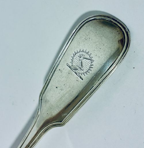 fig 2. A Victorian silver serving spoon displaying a fiddle pattern handle with an engraved crest on the terminal.
