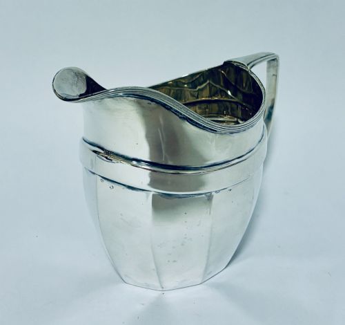 fig 1. An antique polished silver milk jug featuring a faceted lower body, a shaped pouring spout with reeded rim, and an angular handle.