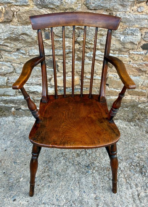 fig 1. An antique dark brown wooden stick back Windsor armchair with turned legs, curved armrests, and a shaped solid elm seat.