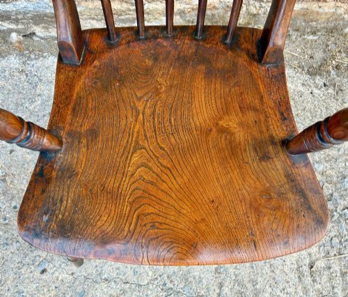 fig 2. An antique dark brown wooden stick back Windsor armchair with turned legs, curved armrests, and a shaped solid elm seat.