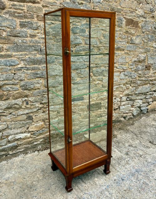 fig 1. A tall, slim mahogany shop display cabinet featuring glass side panels, a single glazed door, three interior glass shelves, and brass catches.