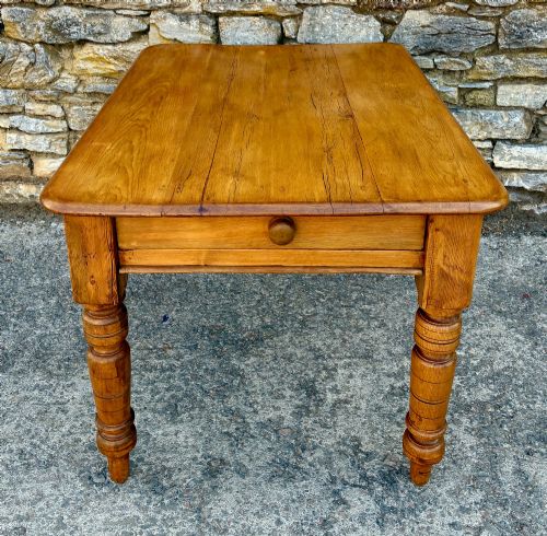 fig 1. An antique pine farmhouse table featuring turned legs, a frieze drawer with a wooden knob, and a warm timber finish.