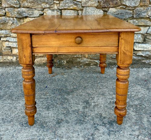 fig 2. An antique pine farmhouse table featuring turned legs, a frieze drawer with a wooden knob, and a warm timber finish.