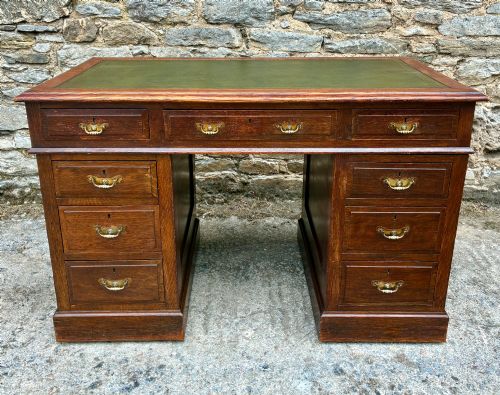 fig 1. An Edwardian oak pedestal desk featuring a green leather writing surface, nine drawers with brass handles, and twin pedestals on plinth bases.