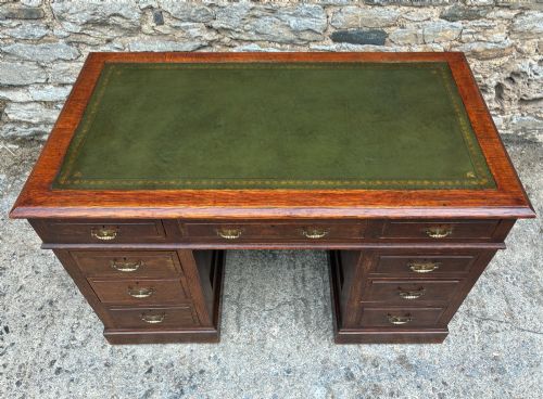 fig 2. An Edwardian oak pedestal desk featuring a green leather writing surface, nine drawers with brass handles, and twin pedestals on plinth bases.