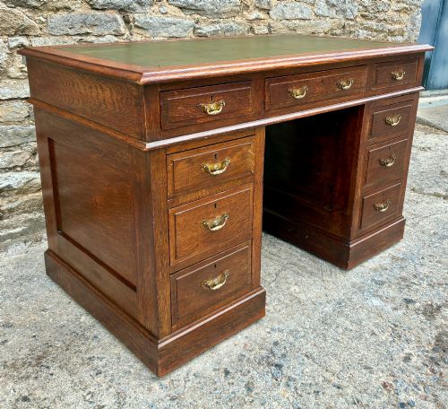 fig 3. An Edwardian oak pedestal desk featuring a green leather writing surface, nine drawers with brass handles, and twin pedestals on plinth bases.