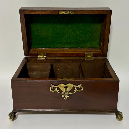 fig 1. A rectangular George III mahogany tea caddy with a stepped lid, top brass swing handle, pierced brass escutcheon with key, and four brass claw-and-ball feet.