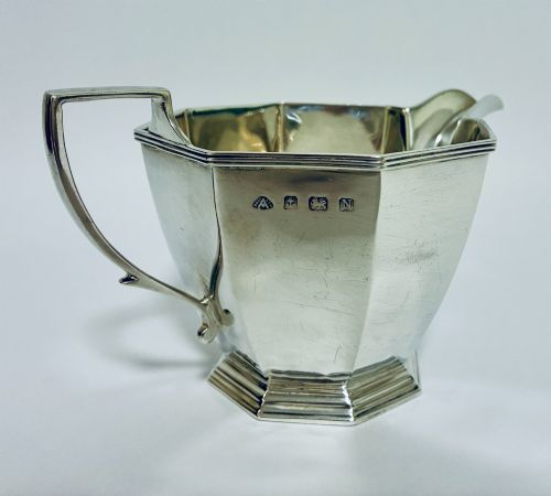 fig 1. An octagonal sterling silver milk jug featuring an angular handle, a pronounced pouring spout, and visible stamped hallmarks on the front facet.