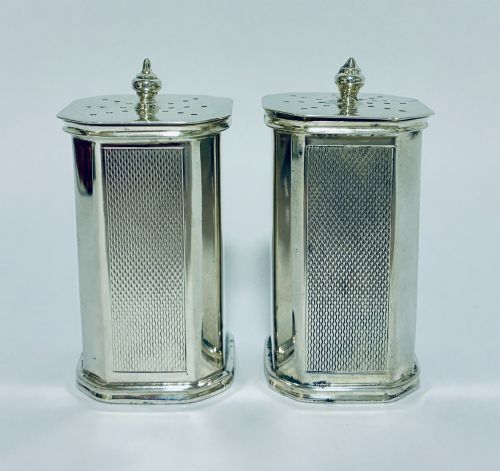fig 1. A pair of matching silver pepper pots with canted corners, engine-turned central panels, and perforated tops with decorative finials.