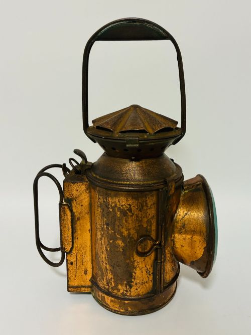 fig 1. An antique metal railway signalling lamp with an arched top carrying handle, a conical vented cap, and a prominent circular glass lens.