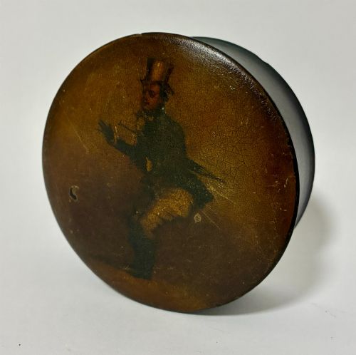 fig 1. A circular Georgian papier-mache table snuff box featuring a hand-painted depiction of a gentleman in a top hat and tailcoat against a dark lacquered background.