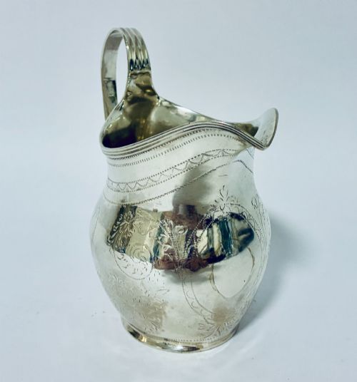 fig 1. A Georgian sterling silver cream jug featuring a high loop handle, a shaped spout, and fine floral engraving across the body.