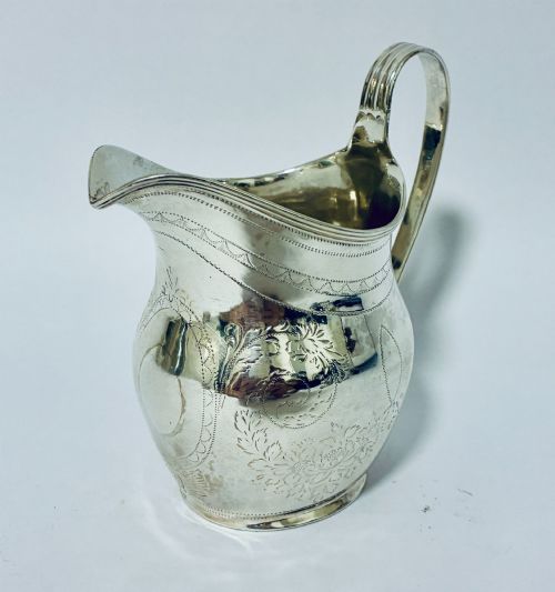 fig 2. A Georgian sterling silver cream jug featuring a high loop handle, a shaped spout, and fine floral engraving across the body.