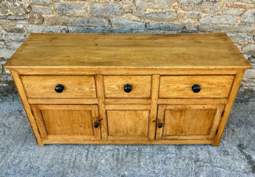 fig 1. A nineteenth-century pine dresser base featuring three top drawers, three lower panelled cupboard doors, and turned dark wooden knobs.