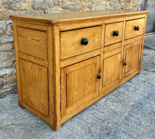 fig 2. A nineteenth-century pine dresser base featuring three top drawers, three lower panelled cupboard doors, and turned dark wooden knobs.