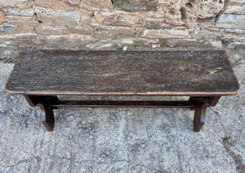 fig 1. A long antique dark wooden hall bench featuring a flat plank seat, shaped slab end supports, and a lower wooden stretcher.
