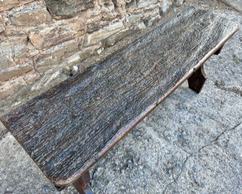 fig 2. A long antique dark wooden hall bench featuring a flat plank seat, shaped slab end supports, and a lower wooden stretcher.