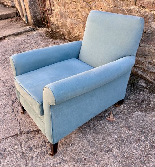 fig 1. An Edwardian deep-seated armchair upholstered in light blue woven fabric with scrolled arms and dark wood legs on brass castors.
