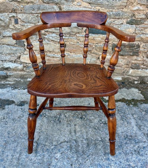 fig 1. A Victorian elm captains armchair featuring a curved horseshoe rail, turned wooden spindles, and a deeply contoured saddle seat showing prominent wood grain.