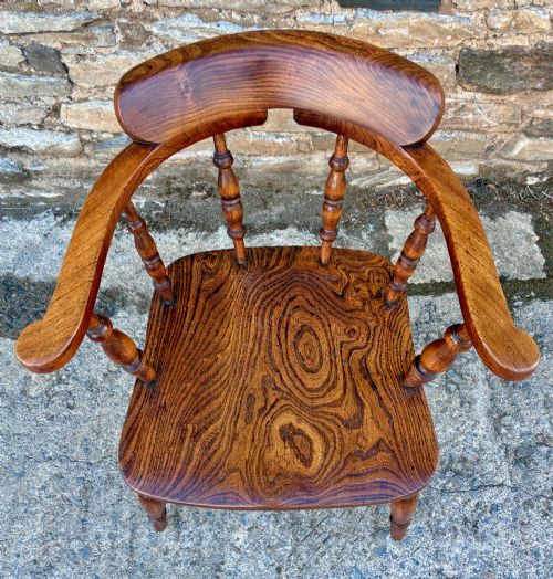 fig 2. A Victorian elm captains armchair featuring a curved horseshoe rail, turned wooden spindles, and a deeply contoured saddle seat showing prominent wood grain.