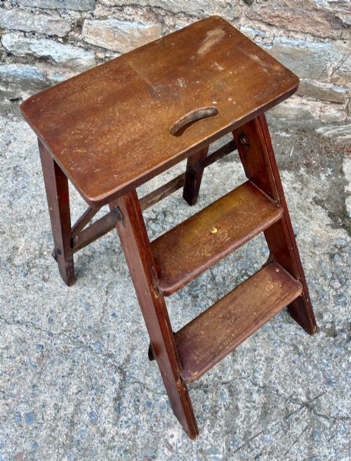 fig 1. A vintage wooden folding step stool with three tread steps and metal side bracing finished in a warm reddish-brown stain.