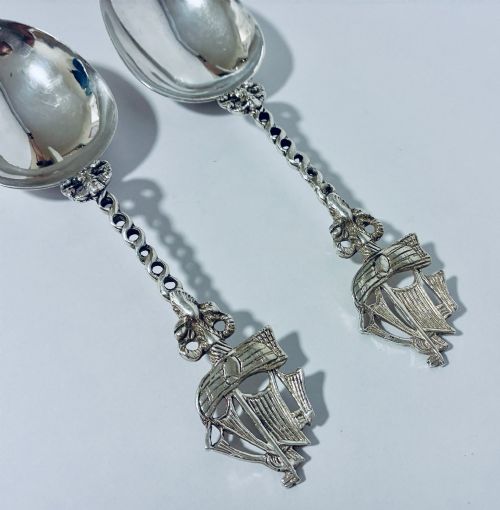 fig 1. A pair of antique silver spoons featuring oval bowls, decorative spiral stems, and detailed sailing ship finials displayed against a plain background.