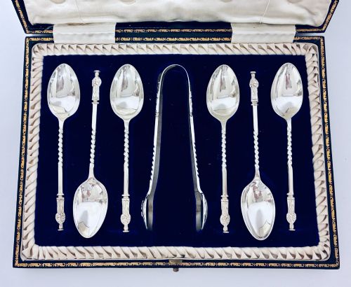 fig 1. An open dark fitted presentation case lined with white satin and blue velvet containing six silver apostle teaspoons with twisted stems and matching silver sugar tongs.