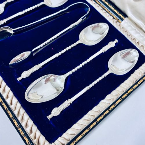 fig 2. An open dark fitted presentation case lined with white satin and blue velvet containing six silver apostle teaspoons with twisted stems and matching silver sugar tongs.
