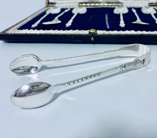 fig 3. An open dark fitted presentation case lined with white satin and blue velvet containing six silver apostle teaspoons with twisted stems and matching silver sugar tongs.