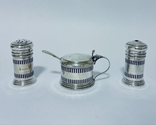 fig 1. An antique three-piece silver cruet set featuring pierced vertical slot details, a mustard pot with lid and spoon, and two matching pepper casters.