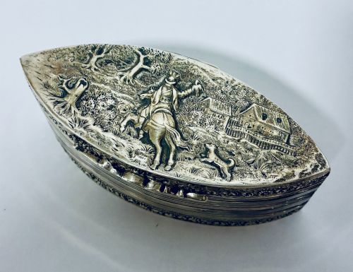 fig 1. An oval silver snuff box featuring a relief equestrian scene on the hinged lid and reeded side walls with carved scroll borders.