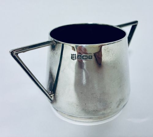 fig 1. A polished sterling silver Art Deco sugar bowl with sharp triangular side handles and visible hallmarks stamped on the exterior wall.