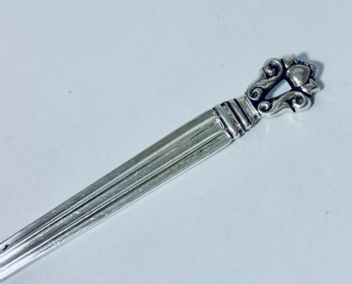 fig 1. A sterling silver ladle featuring a deep bowl, a ribbed tapered handle, and a decorative scroll motif at the terminal.