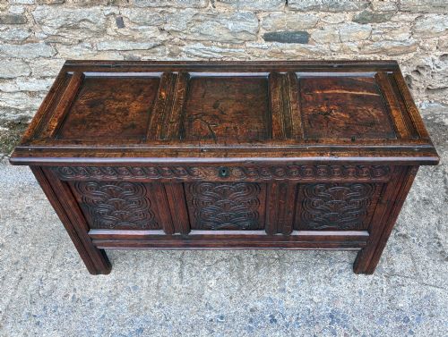 fig 1. A dark oak 17th century coffer featuring a three-panel carved front with geometric scrollwork and a hinged rectangular lid.