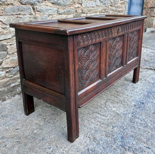 fig 2. A dark oak 17th century coffer featuring a three-panel carved front with geometric scrollwork and a hinged rectangular lid.