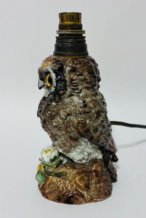 fig 1. A glazed ceramic table lamp base crafted in the shape of an owl with yellow glass eyes, standing on a foliage-adorned base beneath a brass bulb holder.