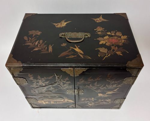 fig 1. An antique Japanese black lacquer table cabinet decorated with gold bird and landscape scenes, fitted with metal corner brackets and a top handle.