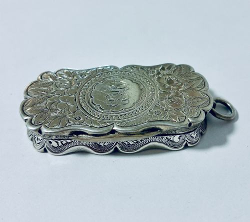 fig 1. A small rectangular Victorian sterling silver vinaigrette featuring hand-engraved floral motifs, a central monogrammed cartouche, scalloped edges, and a side suspension ring.