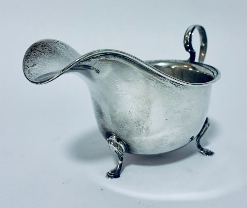 fig 1. An antique silver sauce boat featuring a scrolled flying handle, flared pouring spout, and three cast pad feet.